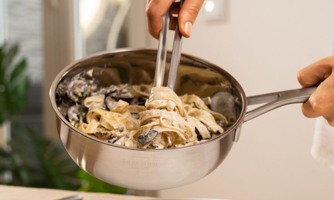 Tagliatelle mit Pilzen in cremiger Sauce werden in einer Sauteuse aus Edelstahl mit der Zange durchgeschwenkt